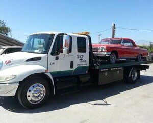 White tow truck carrying a red classic car on a sunny day.