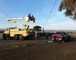 Utility truck with workers in bucket repairing power lines after a car crash.