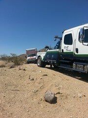Tow truck towing a U-Haul truck in a desert landscape under a clear blue sky.