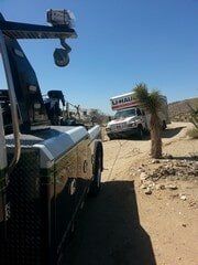 Tow truck pulling a U-Haul truck on a desert road under a blue sky.