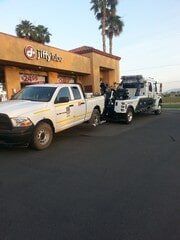 White tow truck towing a white pickup truck in front of Jiffy Juice store.