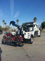 Tow truck with a red motorcycle loaded, in a parking lot under a sunny sky.