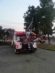 Tow truck lifting a motorcycle. Red, white tow truck, parked outdoors. Dusk setting.
