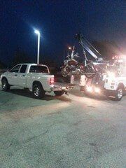 White pickup truck and tow truck with motorcycle being loaded at night.