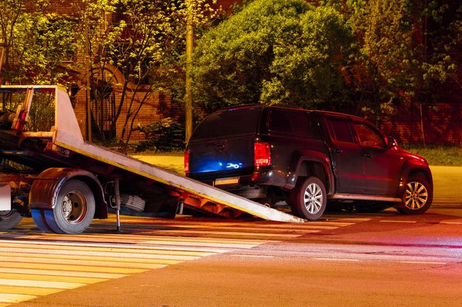 Flatbed tow truck securing a black SUV for nighttime emergency towing.