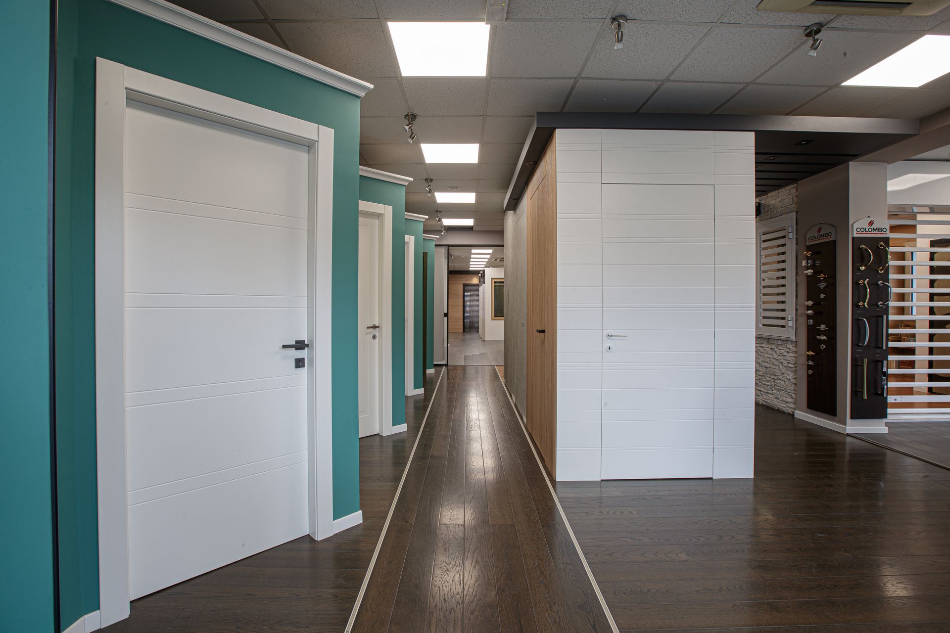 Corridoio interno con porte bianche e pareti color verde acqua che mostrano i diversi stili di porte in uno showroom.