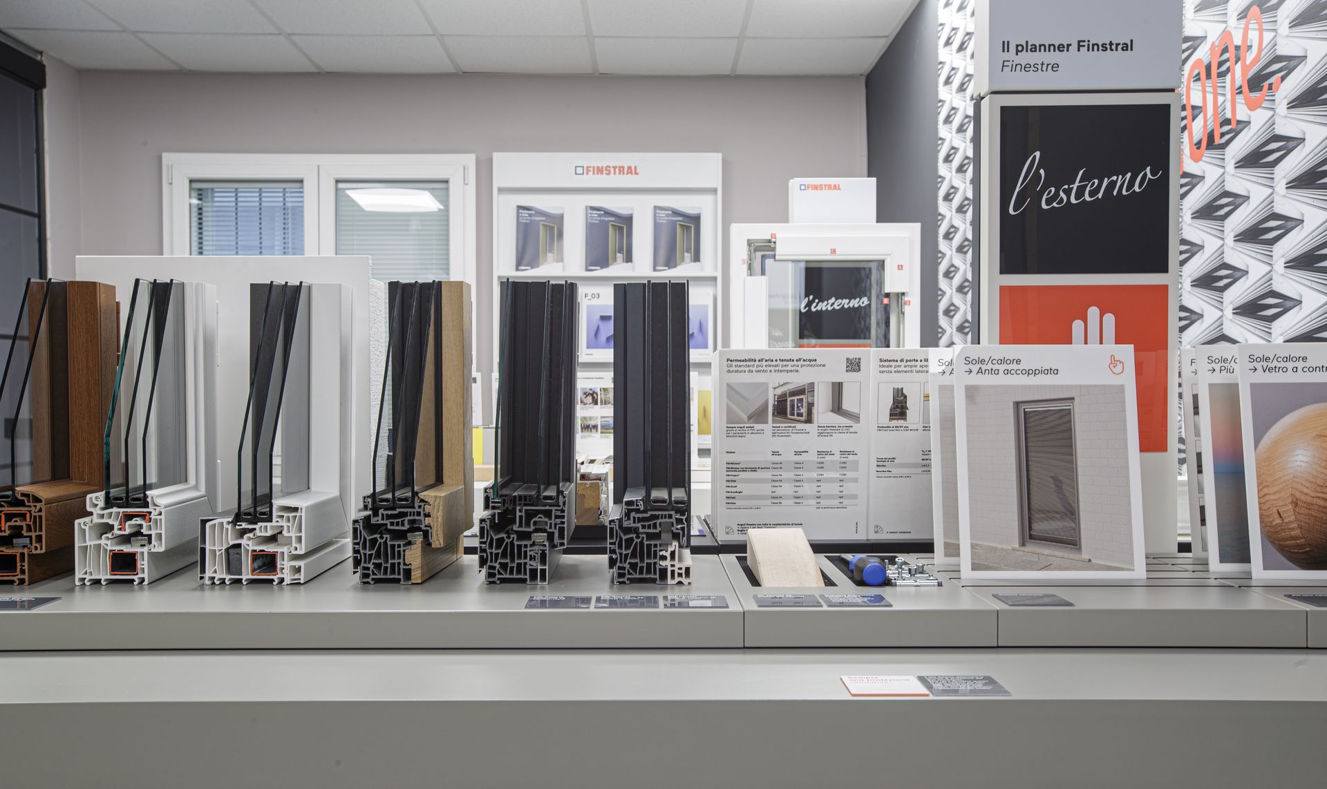 Esposizione di sezioni trasversali di telai di finestre con brochure e informazioni, all'interno di uno showroom.