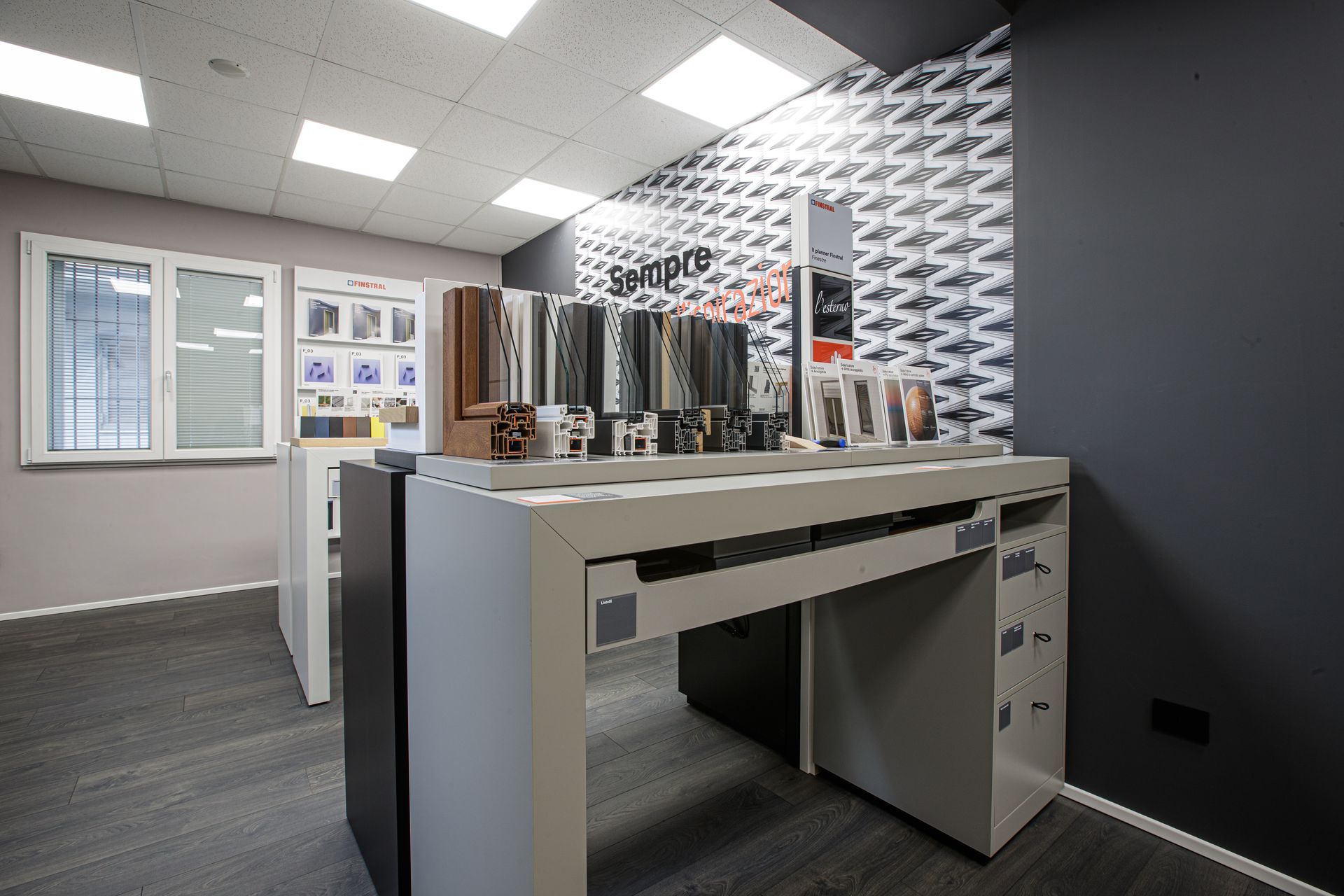 Interno di uno showroom con tavoli espositivi che espongono campioni di finestre e porte.
