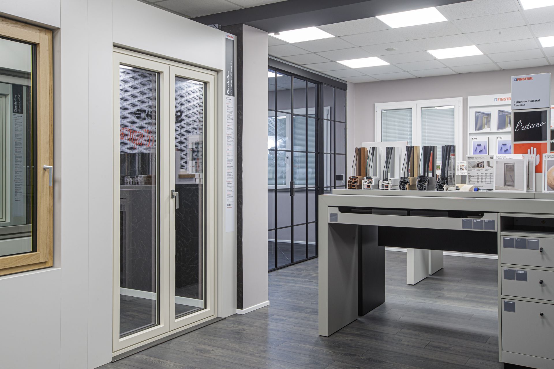 Interno di uno showroom che espone campioni di finestre e porte; combinazione di colori grigio e bianco.