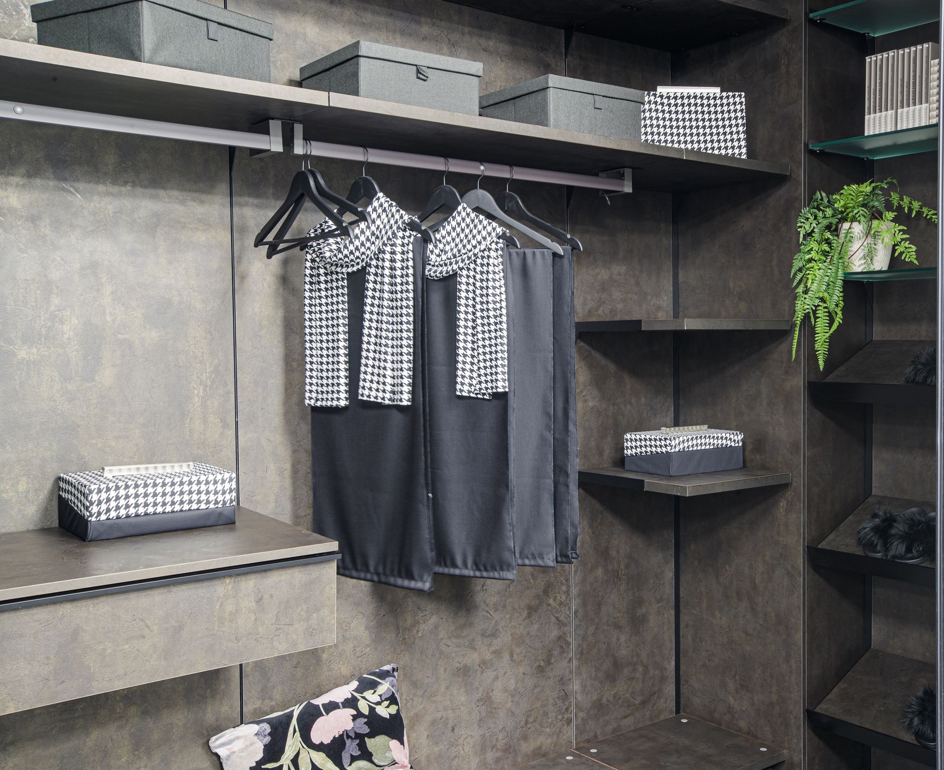 Cabina armadio con ripiani grigio scuro, vestiti appesi, scatole e una pianta.