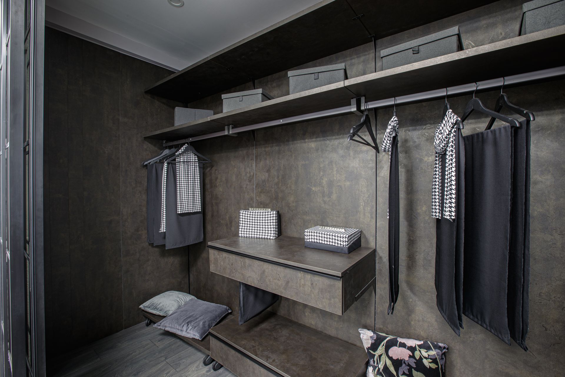 Moderna cabina armadio con pareti, ripiani e abiti appesi scuri; combinazione di colori grigio e nero.