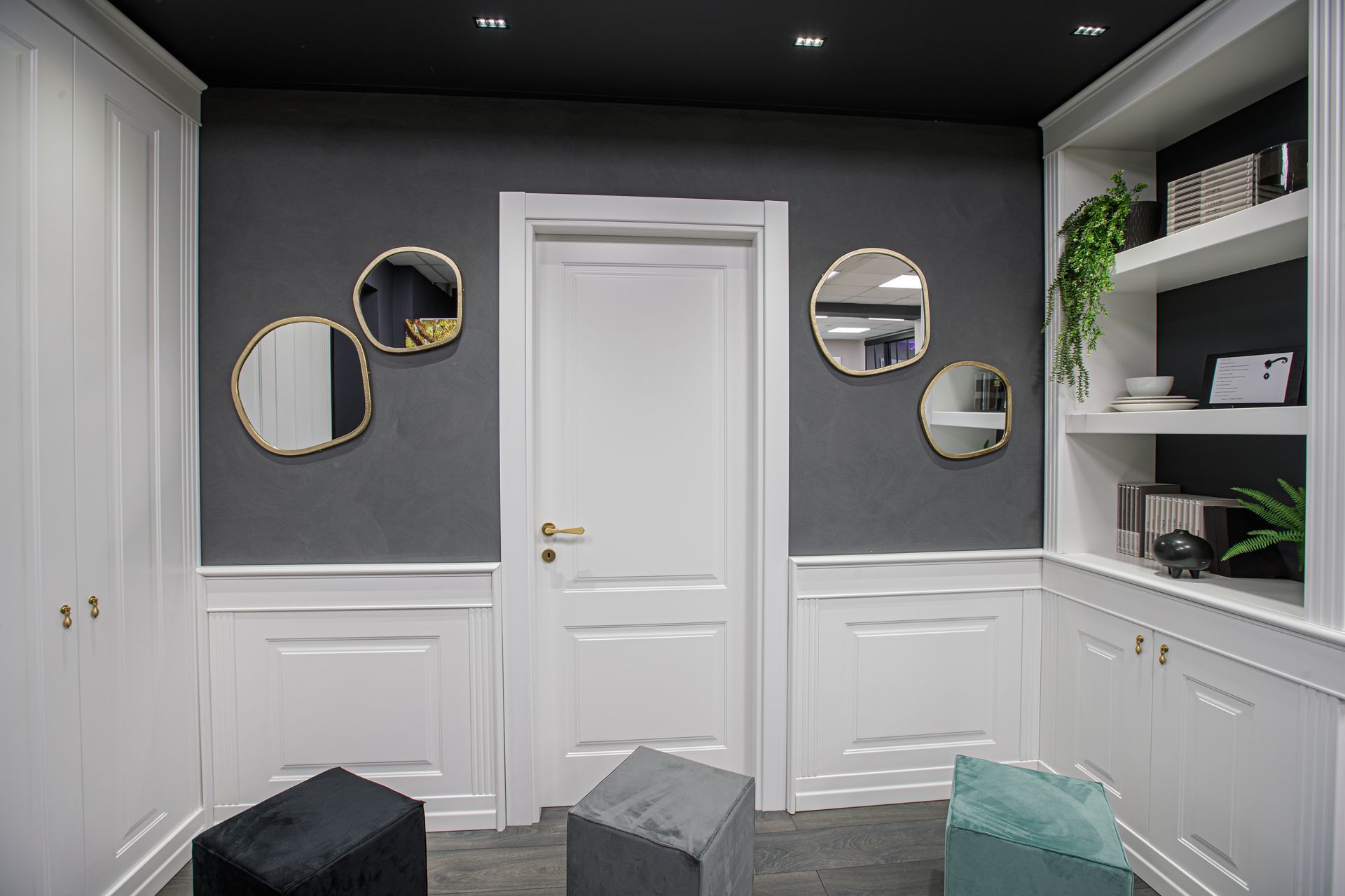 Interno con pannelli bianchi, pareti grigie, specchi con cornice dorata, scaffalature integrate e soffitto nero.