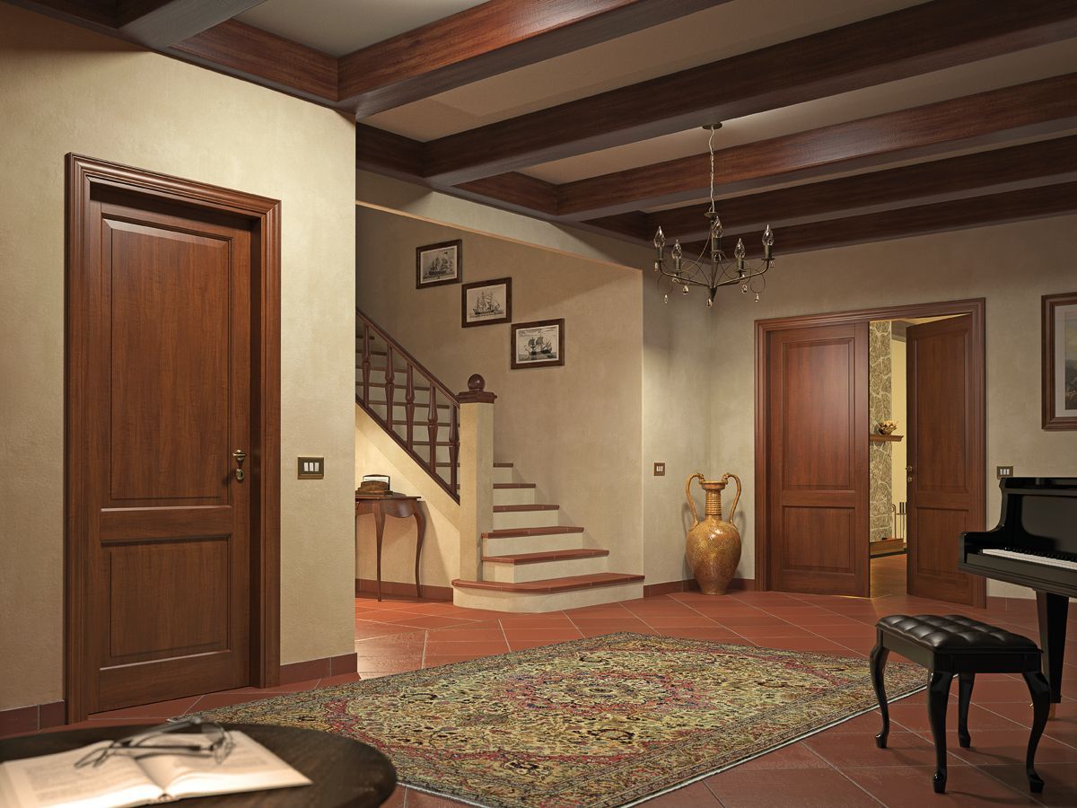 Un interno illuminato in modo caldo, con una scala, diverse porte in legno e un pianoforte su un pavimento piastrellato con un tappeto a motivi.