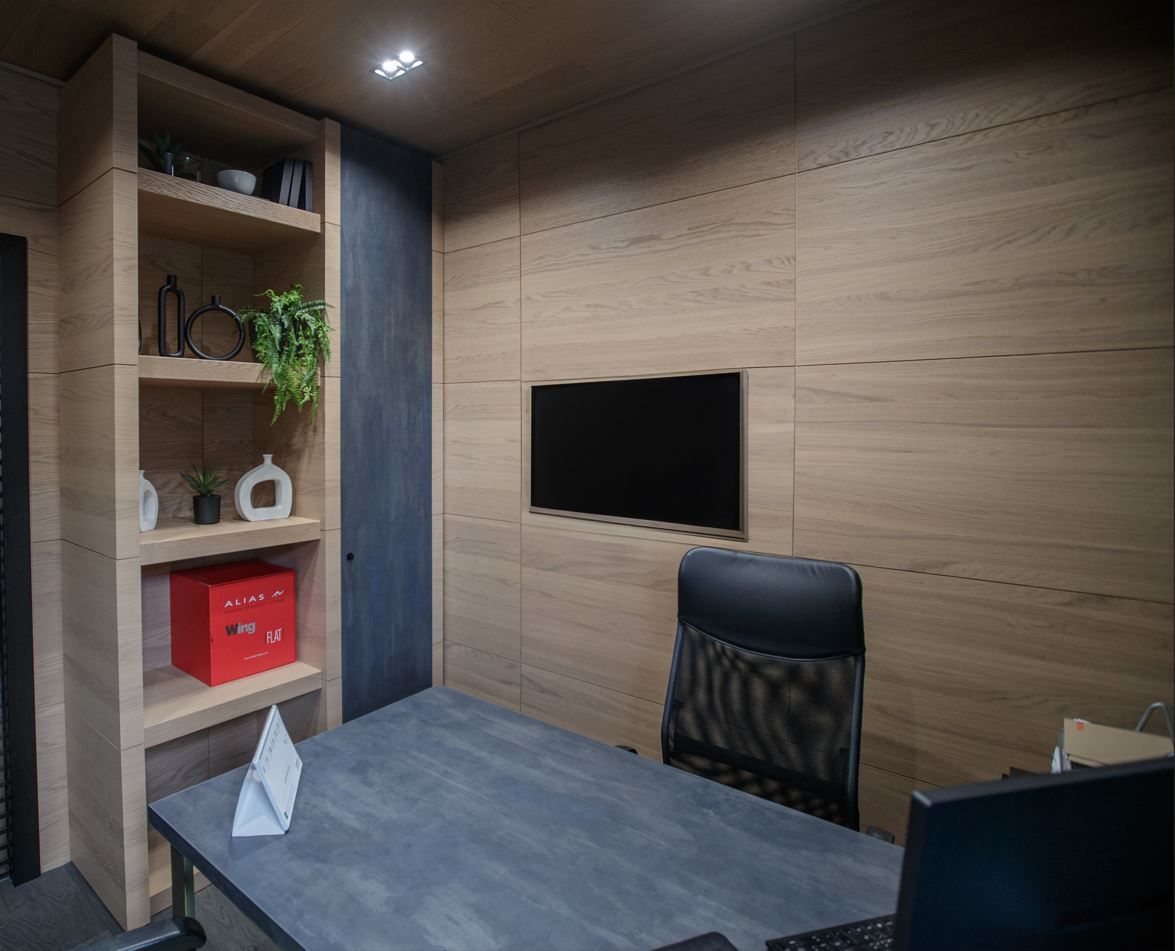 Ufficio con pareti in legno, scrivania, scaffali decorati e uno schermo.