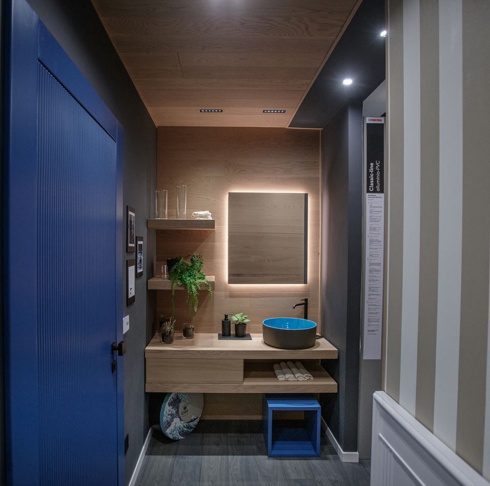 Bagno con porta blu, pannelli in legno, mensole sospese, lavandino rotondo blu e parete a strisce.