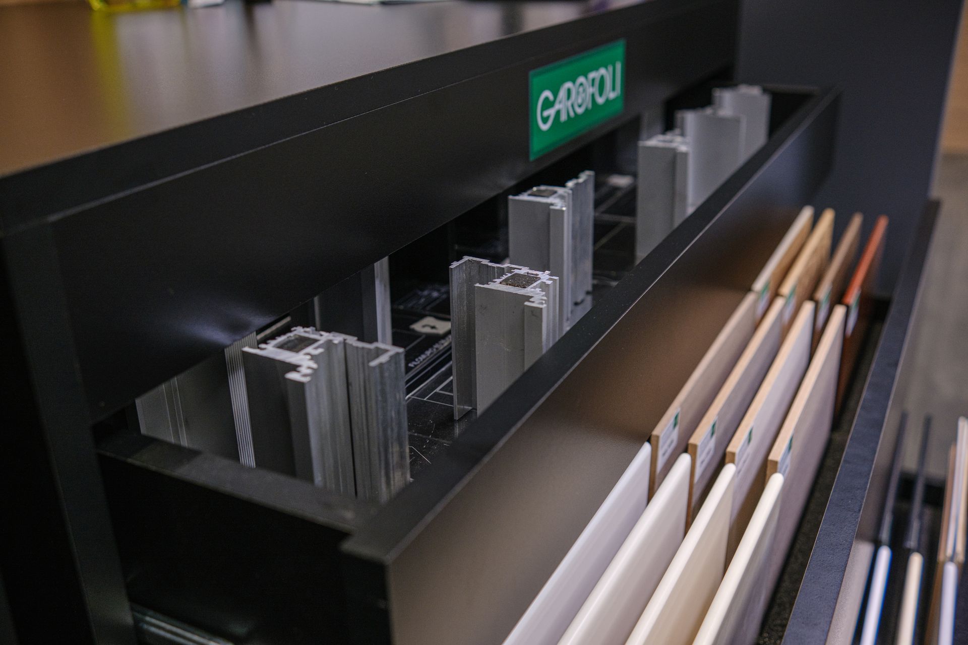 Vetrina nera con campioni di alluminio e legno. È visibile il logo del marchio G-RIMOLI.