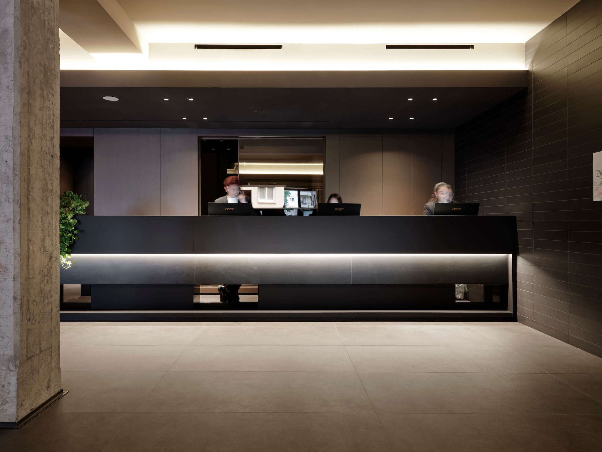 Reception dell'hotel con tre membri dello staff, arredamento scuro e bancone illuminato.