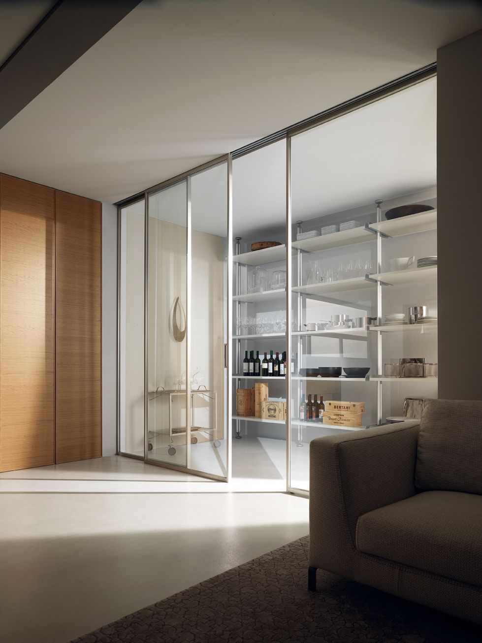 Le porte scorrevoli in vetro rivelano una moderna dispensa con ripiani per gli utensili da cucina. Sono visibili anche una parete in legno e un divano.
