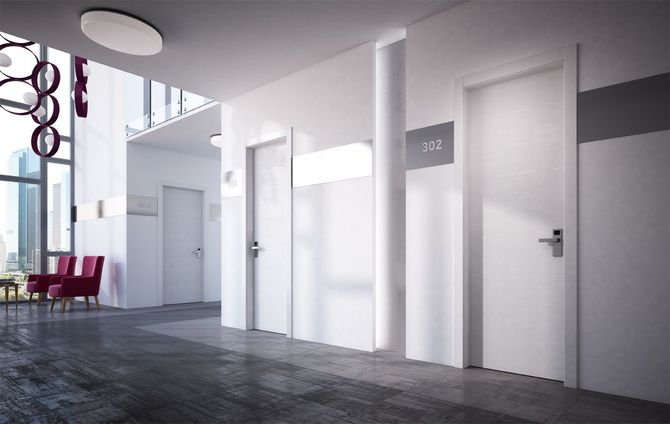 Corridoio con tre porte bianche, una delle quali reca il numero della stanza. Una finestra sulla sinistra.