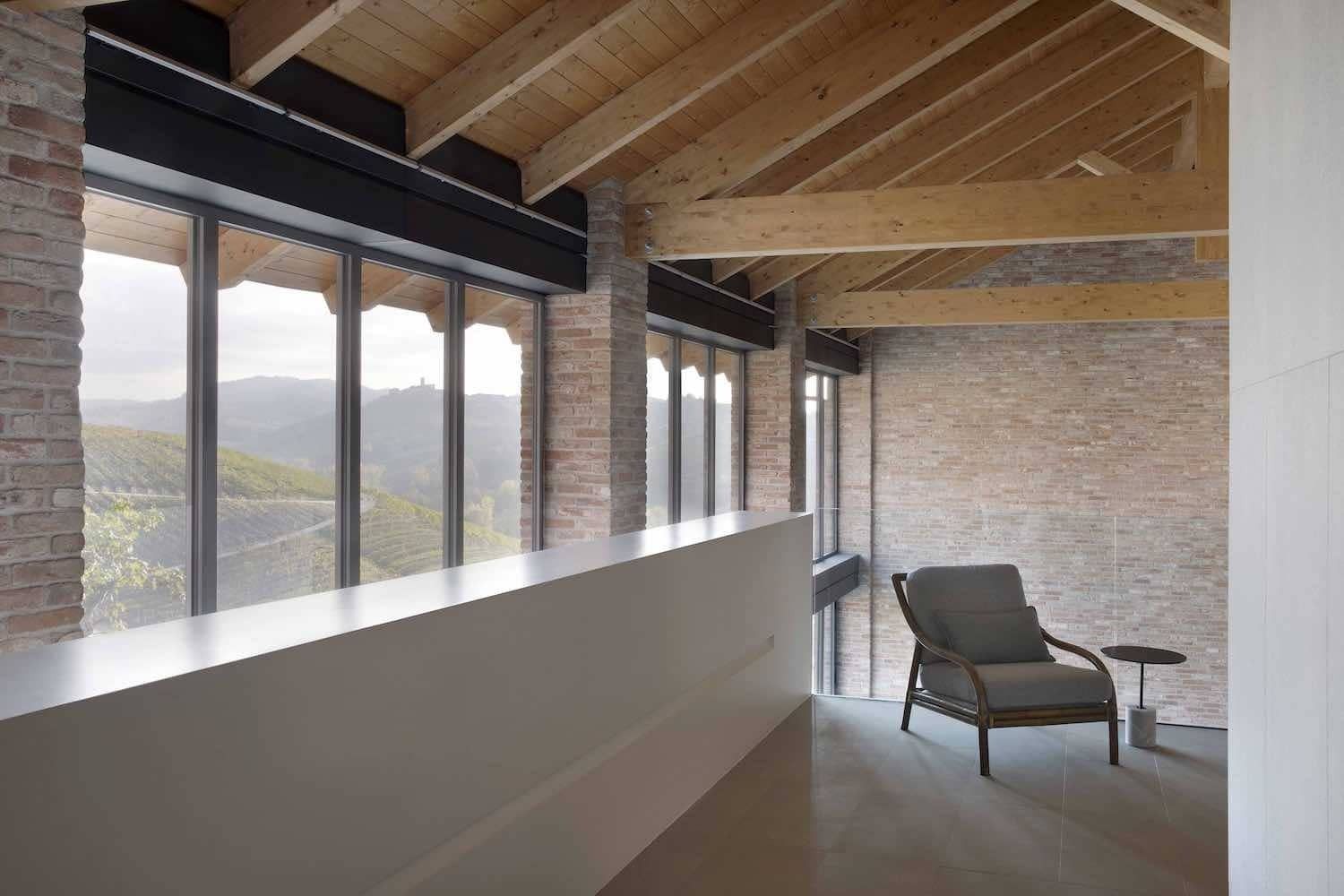 Interno con pareti in mattoni, travi in ​​legno, grandi finestre, ringhiera bianca e una sedia.