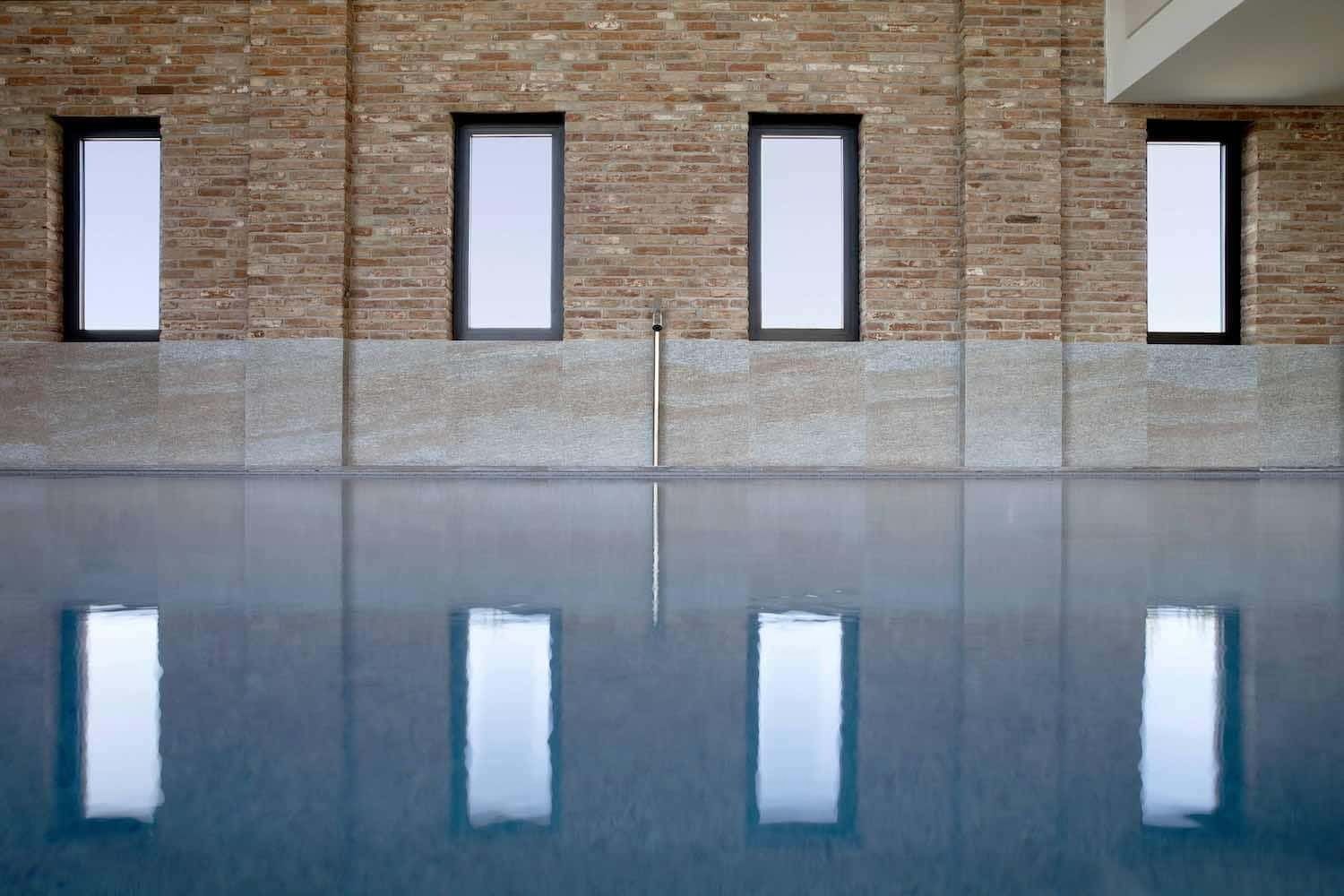 Piscina con quattro alte finestre che si riflettono nell'acqua, contro un muro di mattoni.