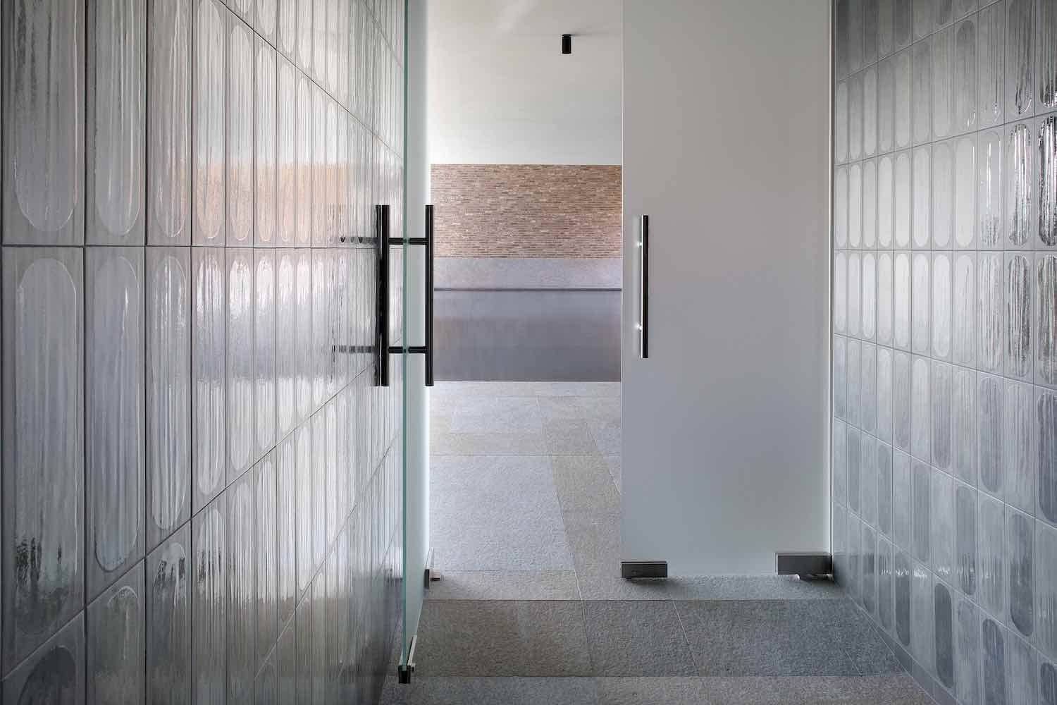 Ingresso in vetro con pareti strutturate e porta aperta che conduce a una stanza con una parete in mattoni.