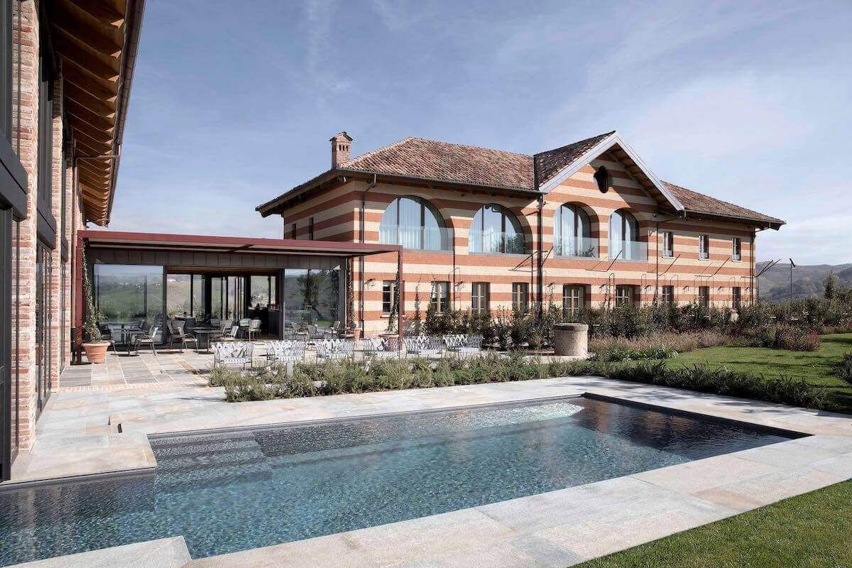Casa di lusso con piscina e veranda, esterni in mattoni rossi, immersa in un paesaggio soleggiato e verdeggiante.