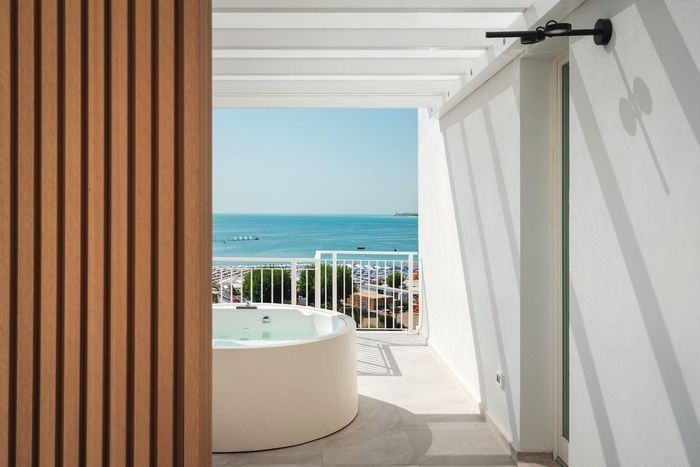 Un balcone con vasca idromassaggio e vista sull'oceano. Pareti bianche, doghe in legno e acqua azzurra.