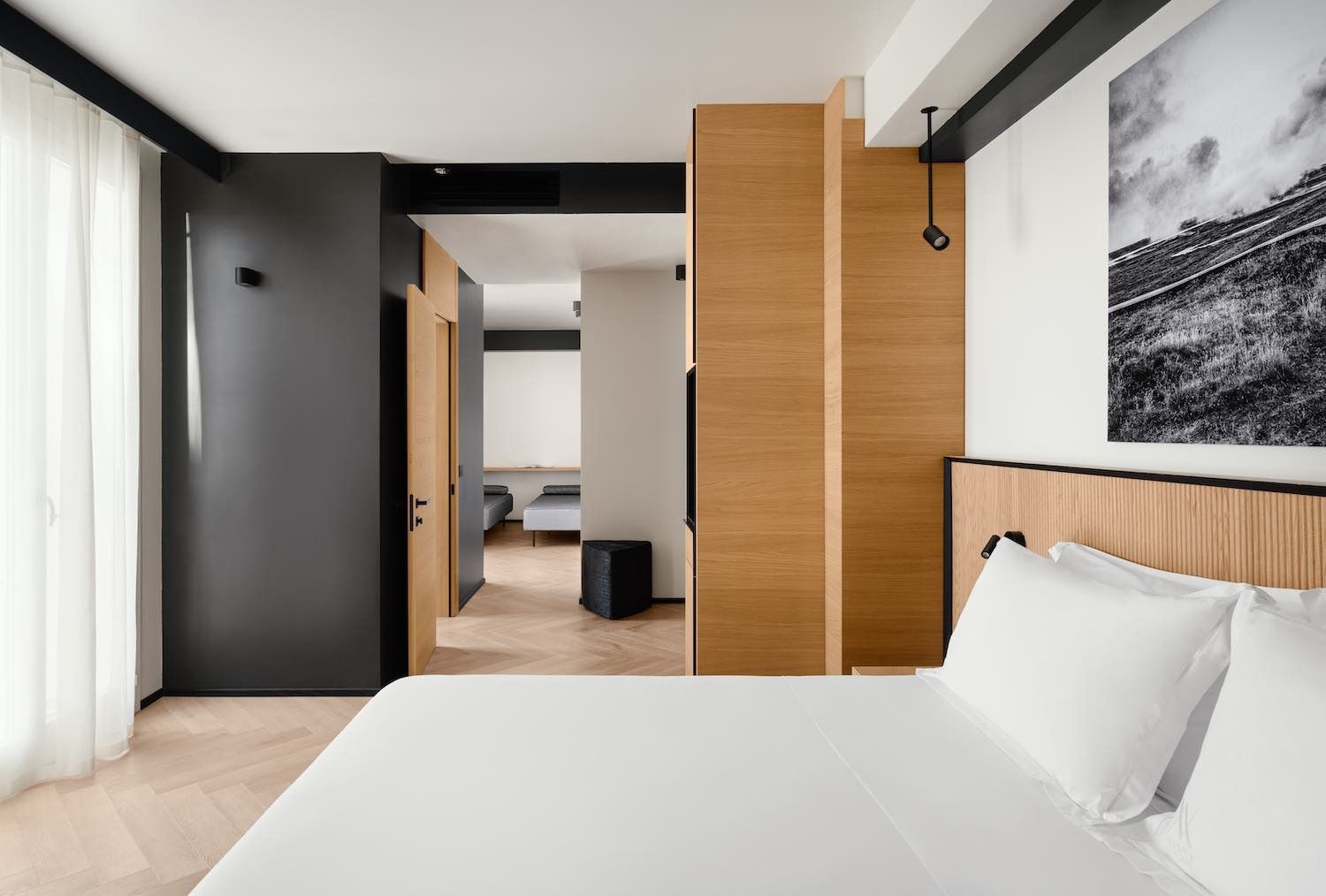 Moderna camera d'albergo con letto, pannelli in legno e vista su un'altra stanza.