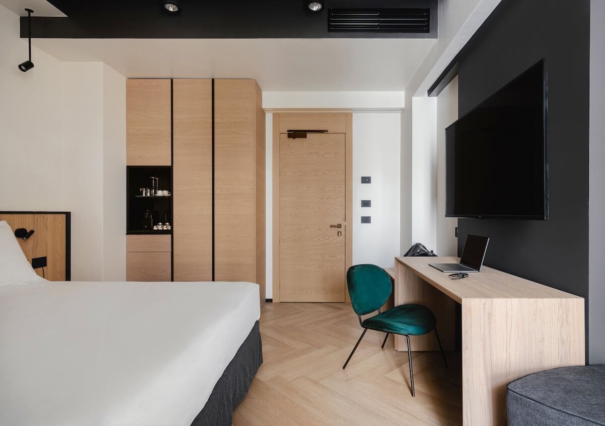 Moderna camera d'albergo con letto, scrivania, TV, armadio in legno e sedia color verde acqua.