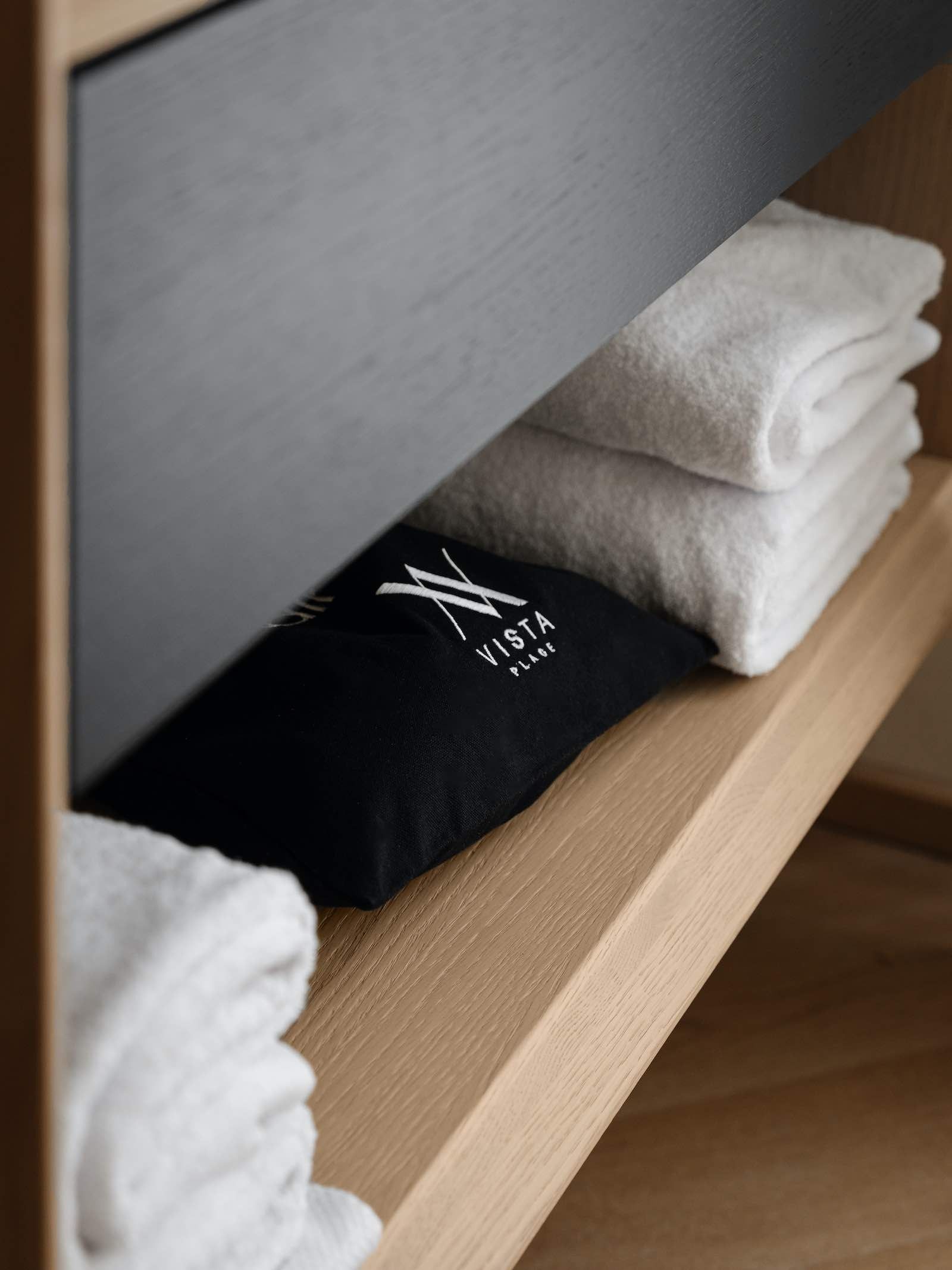 Mensola in legno con asciugamani bianchi e neri impilati. L'asciugamano nero ha il logo bianco.