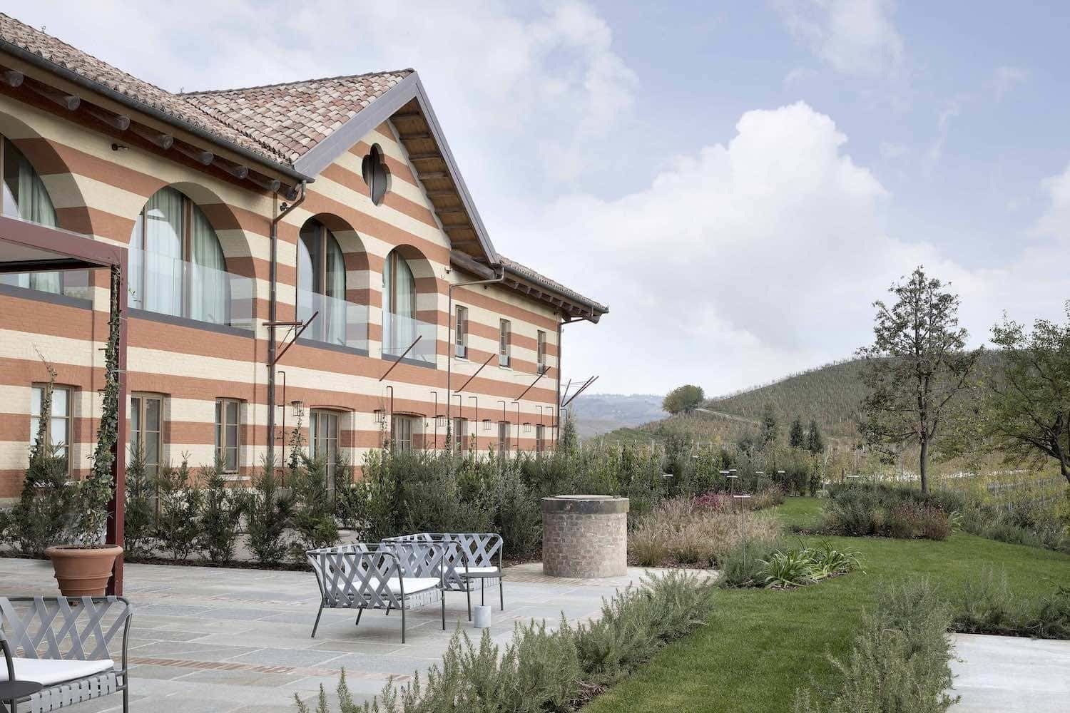 Terrazza di un edificio con facciata a strisce, due sedie e giardino con vista su una collina sotto un cielo nuvoloso.