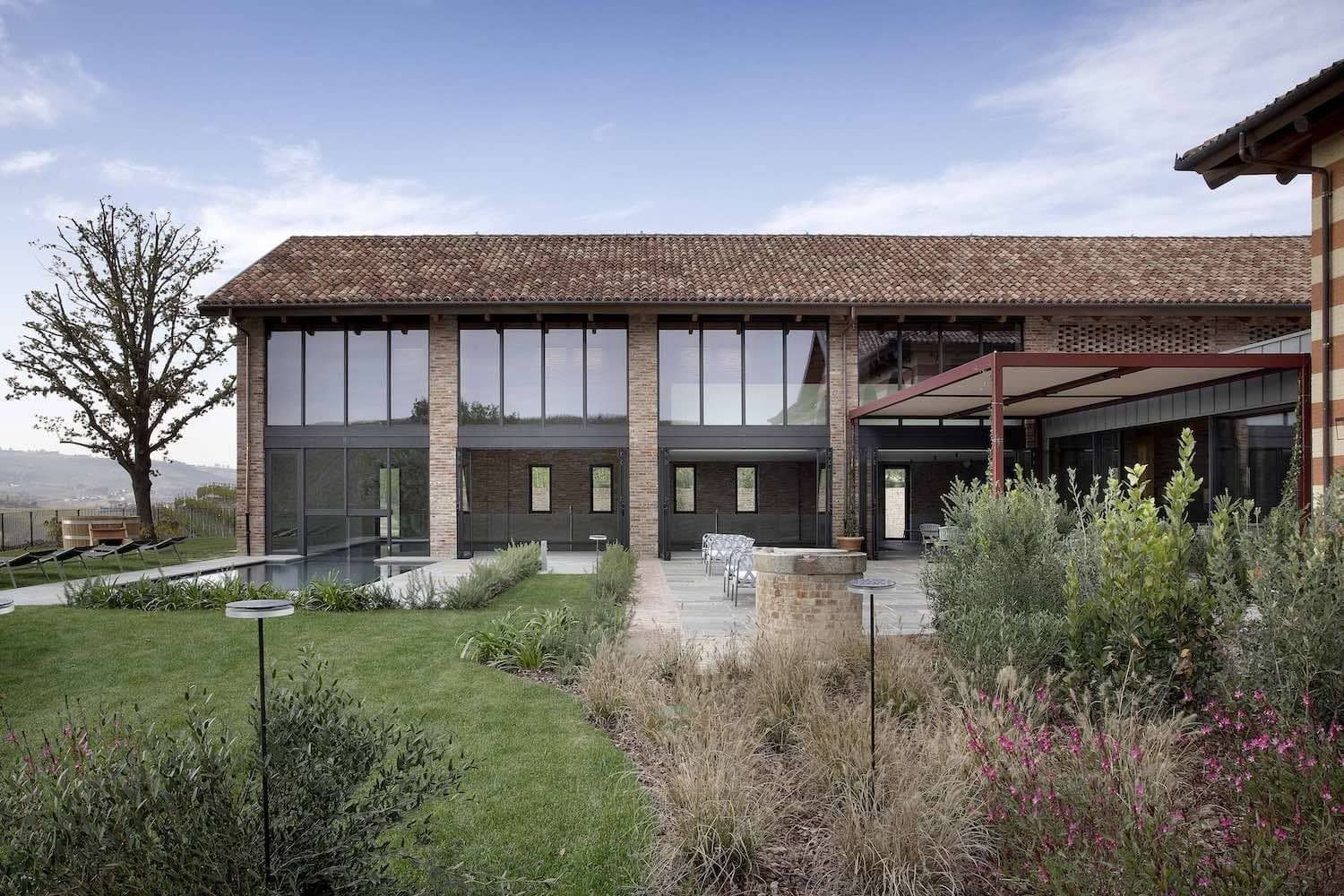 Edificio moderno con ampie finestre e tetto di tegole rosse, circondato da erba verde e piante.