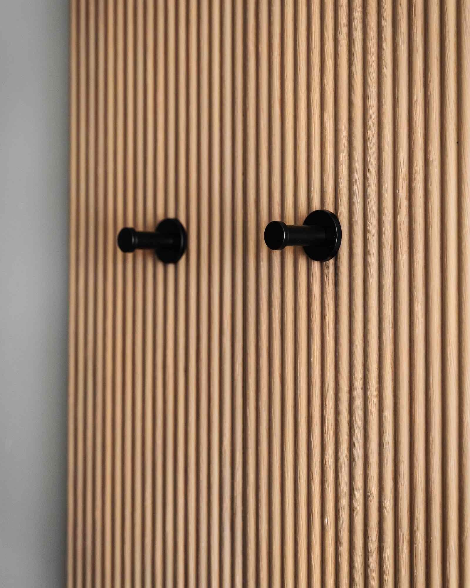 Due ganci neri su una parete verticale con doghe in legno chiaro.