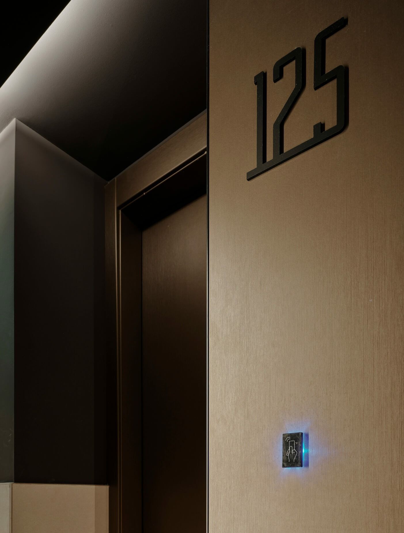 Stanza 125 con numeri in metallo scuro, porta marrone e pannello di accesso.