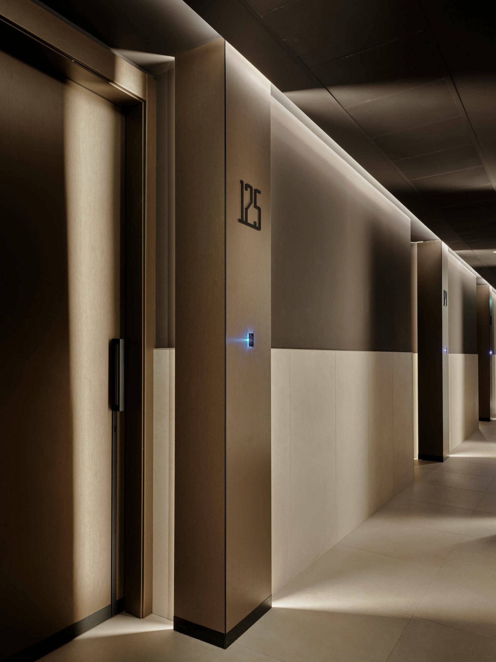 Corridoio dell'hotel con la stanza 125. Pareti color tortora, porte scure e illuminazione da incasso.