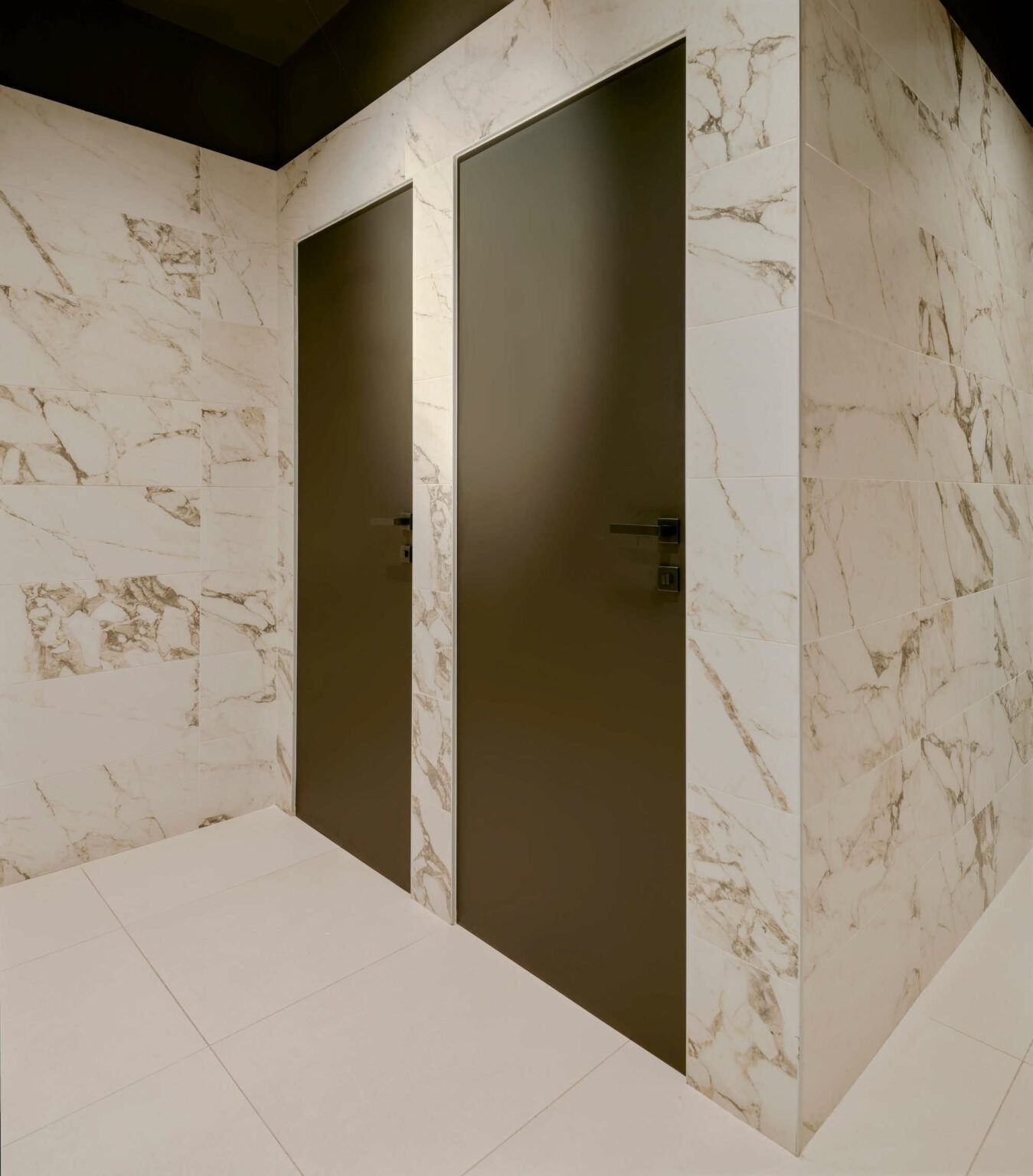 Due porte marrone scuro in un bagno rivestito di marmo.