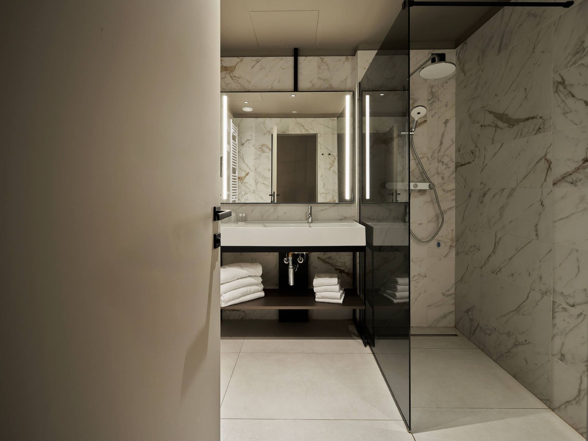 Bagno moderno con pareti in marmo, doccia in vetro e lavandino bianco.