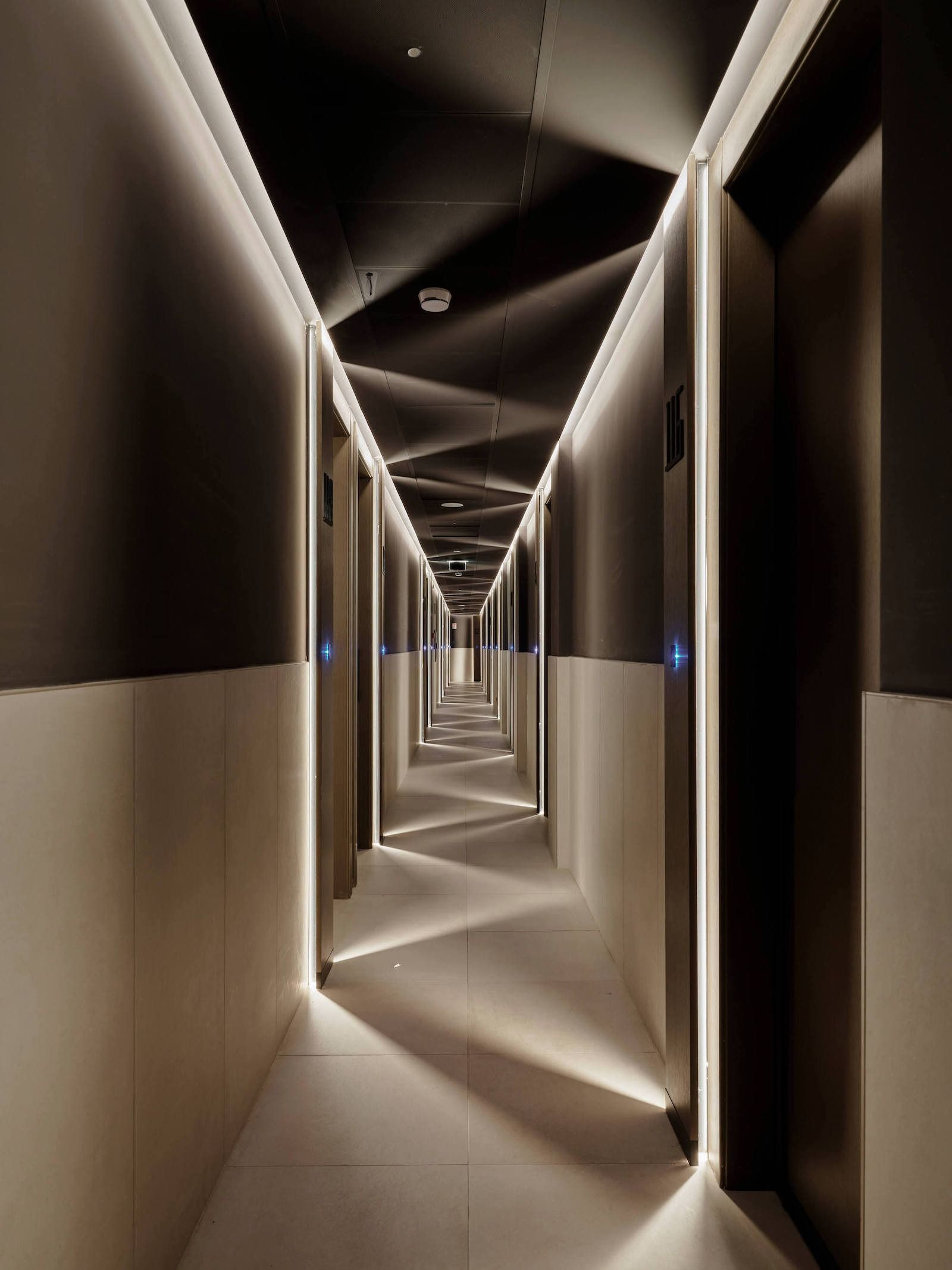 Lungo corridoio dell'hotel con soffitto angolato e illuminato e porte lungo i lati.
