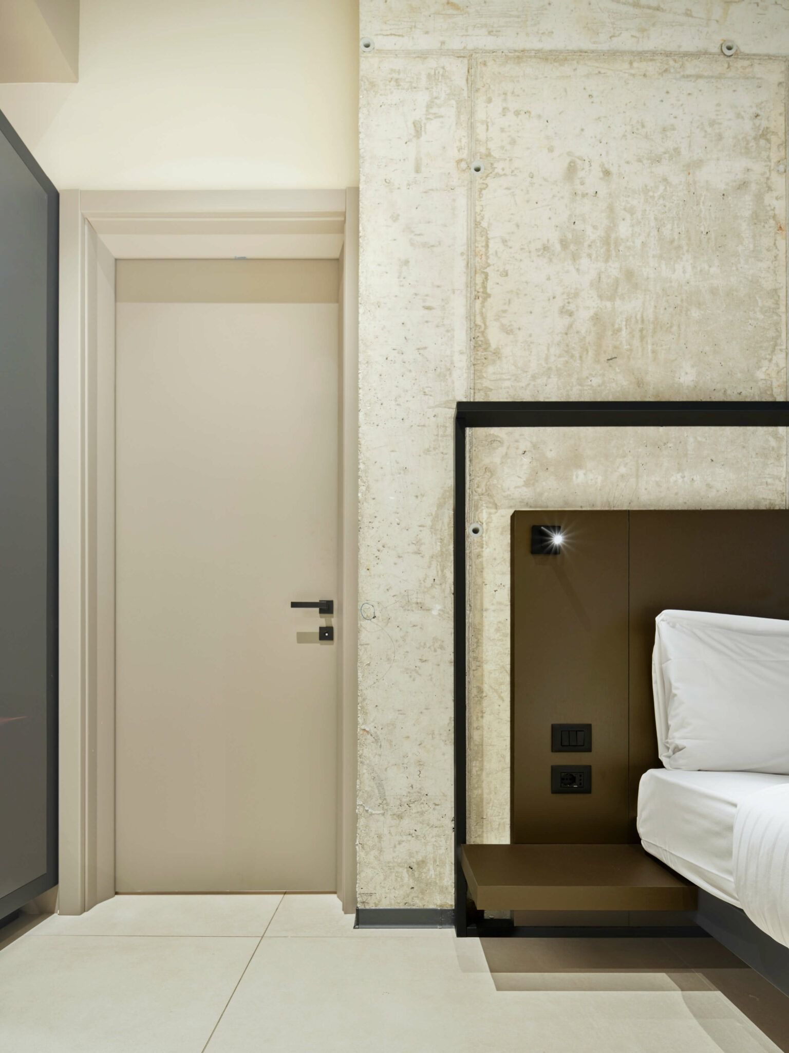 Camera da letto con letto, porta, parete in cemento e testiera moderna con luci.