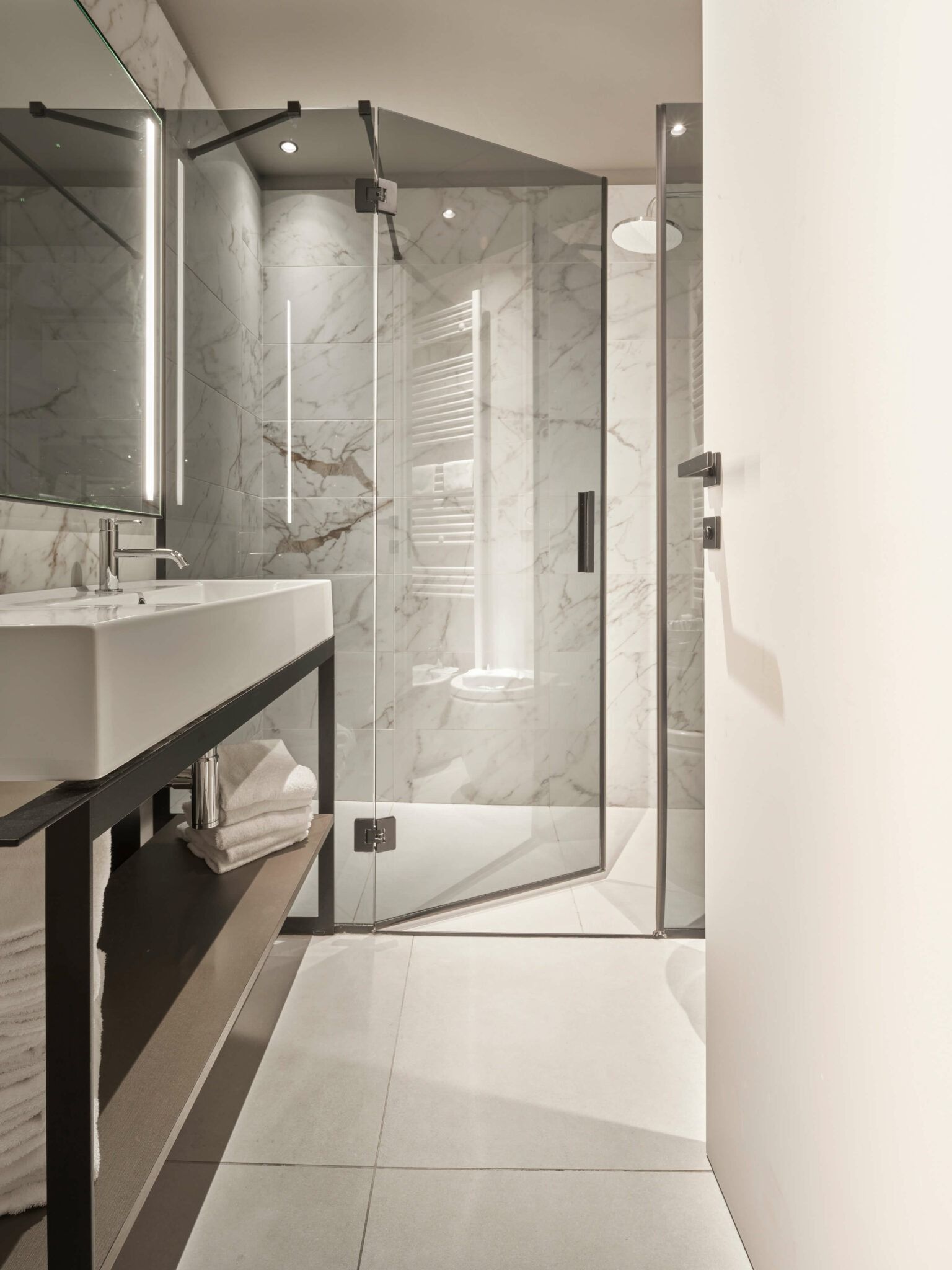 Bagno moderno con doccia in vetro, pareti in marmo e lavandino bianco.