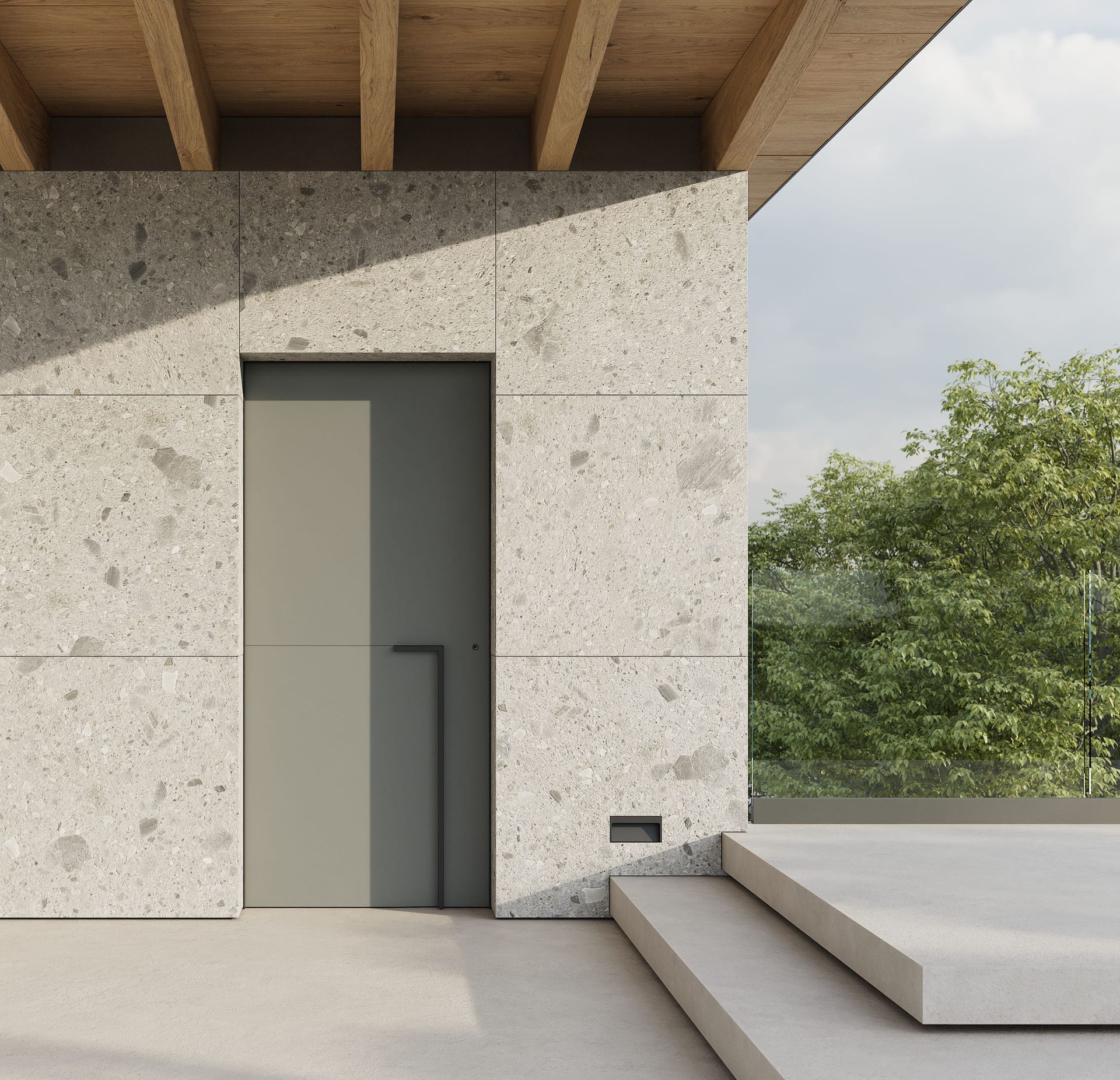 Esterno di un edificio moderno con porta grigia e pareti in pietra ruvida. Soffitto in legno e scorcio di verde.