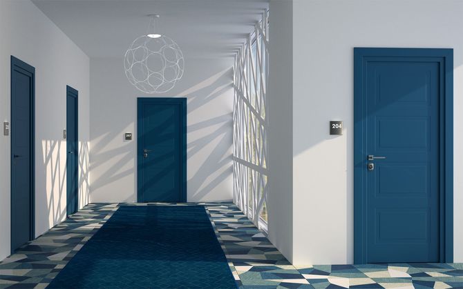 Corridoio con porte e moquette blu, luce naturale e un lampadario decorativo.