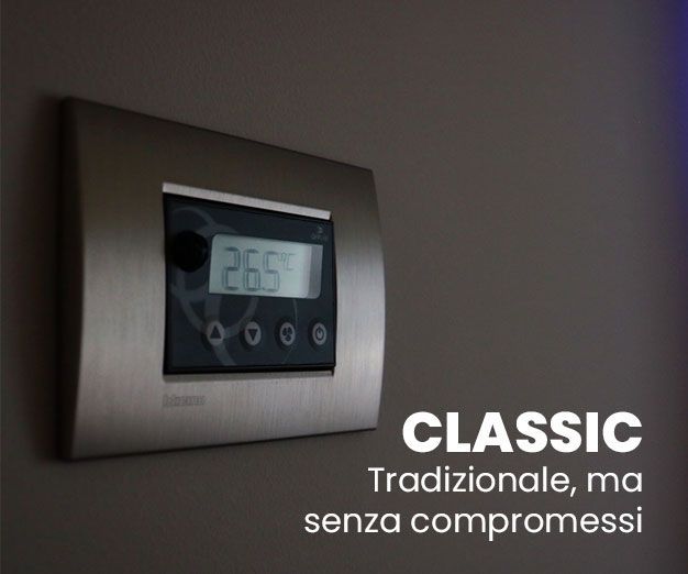 Termostato argentato a parete che indica 26,5°C. Testo 