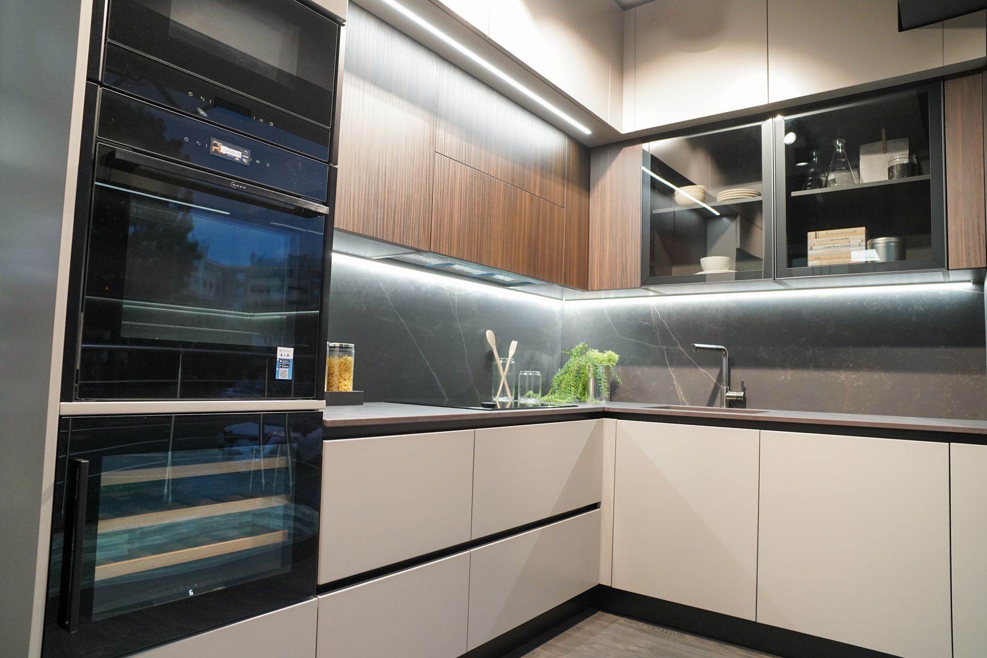 Cucina moderna con elettrodomestici neri, mobili bianchi, pensili in legno e piano di lavoro grigio.