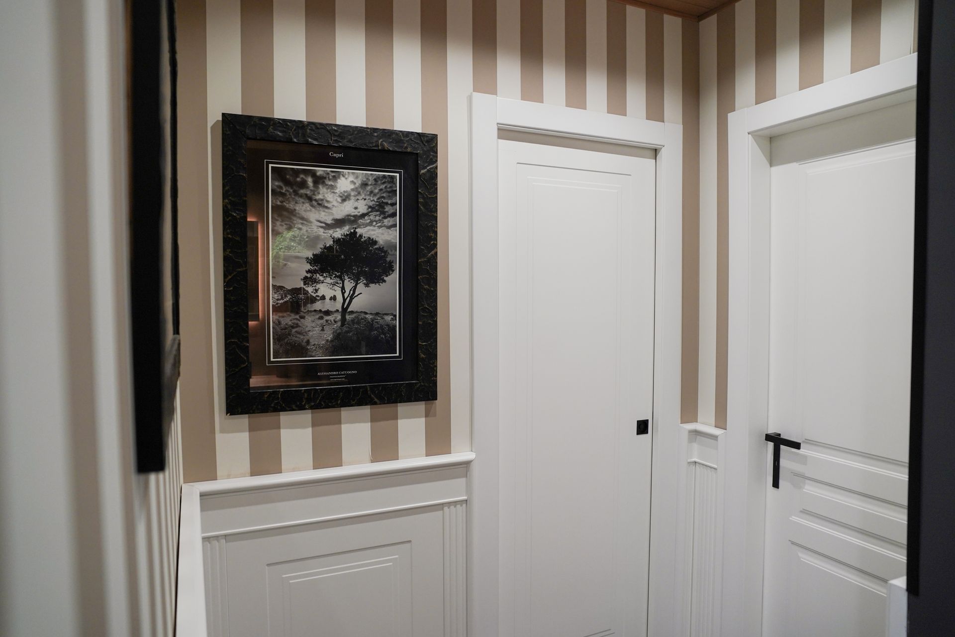 Corridoio con carta da parati a righe, quadri incorniciati e porte bianche con ferramenta nera.