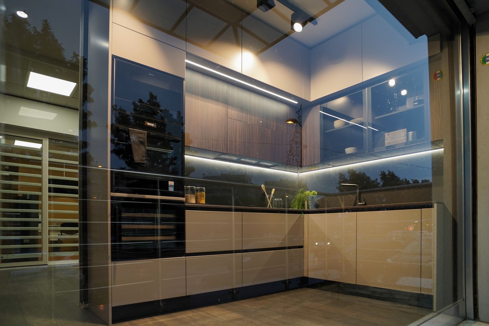 Esposizione di una cucina moderna con vetrine in vetro, illuminazione calda e mobili dai toni neutri.