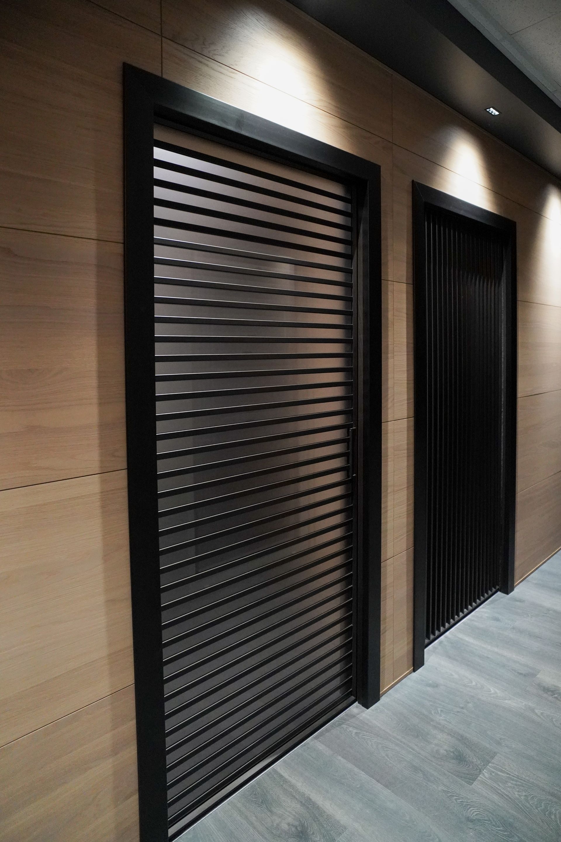 Due porte moderne con cornici nere e pannelli in legno alle pareti. Una porta ha listelli orizzontali.
