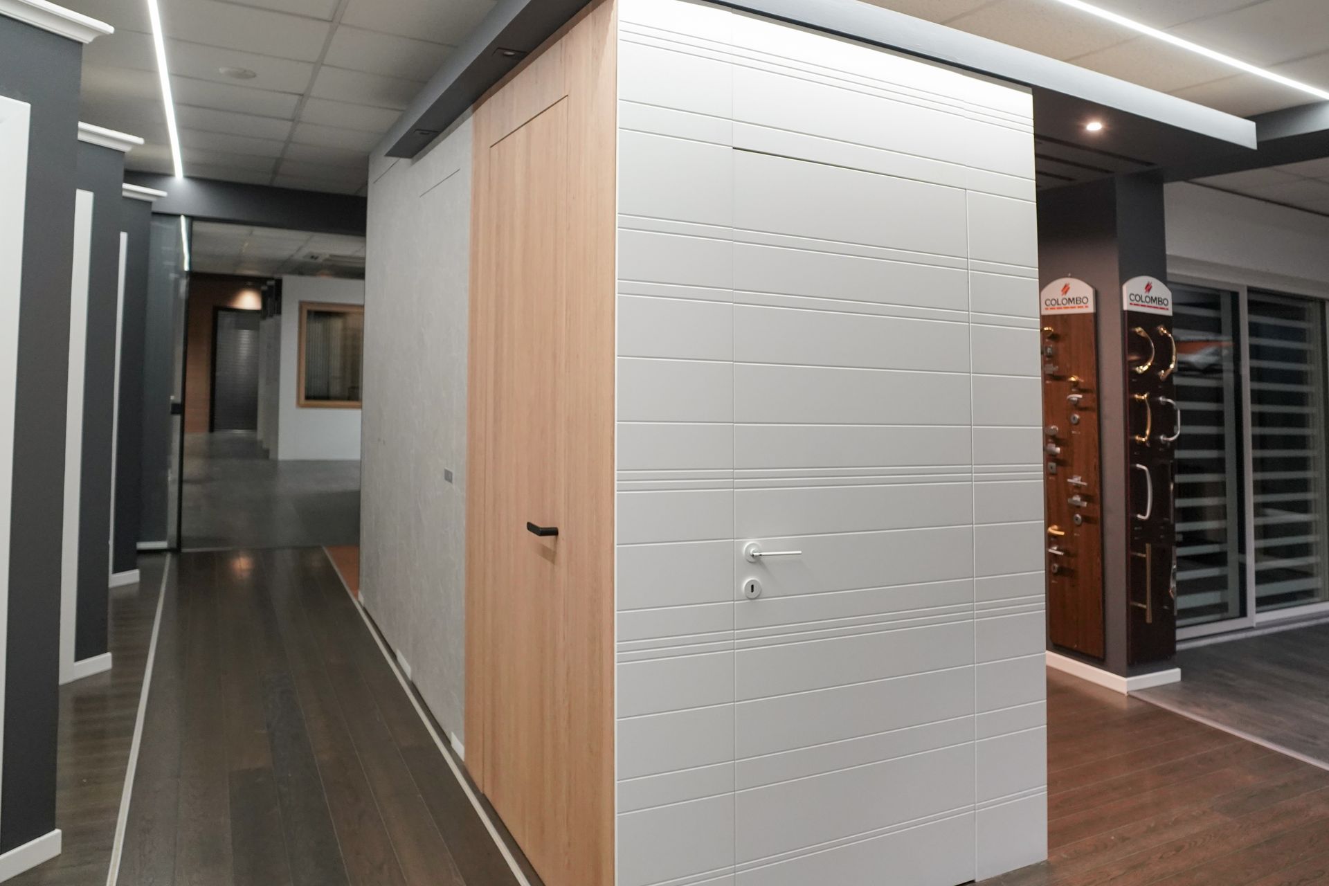 Showroom di porte per interni: porte in legno e bianche esposte, pavimenti in legno scuro, illuminazione da incasso.