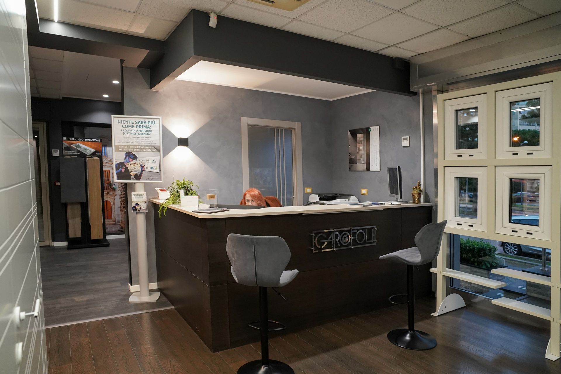 Una zona reception con una scrivania marrone scuro, due sgabelli da bar e campioni di finestre esposti.